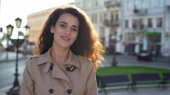 Portrait of Happy Young Woman Wearing Coat Smiling While Strolling Through Morning City Street in