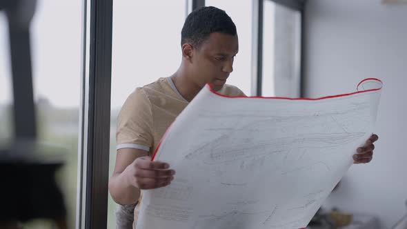 Portrait of Thoughtful Talented African American Architect Analyzing Blueprint in Home Office