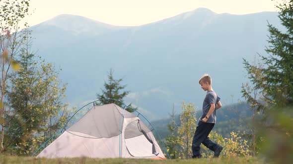 Happy child boy jumping up with raised hands near a camping tent in mountains enjoying view 