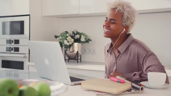 Positive African American Female Smiling Sitting at Table with Laptop in Kitchen