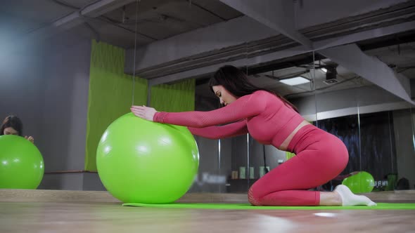 Young Woman in Pink Costume Doing Exercises in the Gym Leaning on the Fitness Ball and Stretching