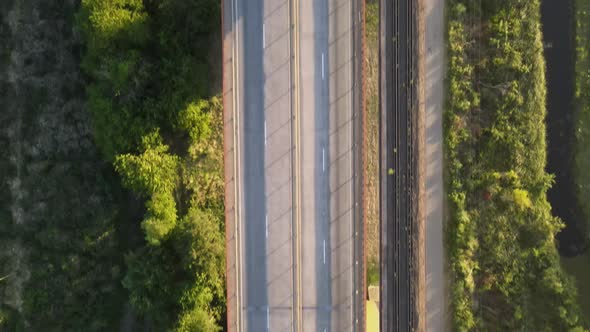 Aerial top down dolly in following a road and railway cable-stayed bridge surrounded by vegetation a