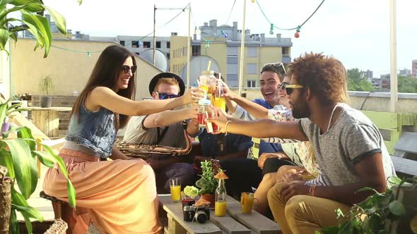 Cheerful multi-ethnic friends laughing and toasting with cocktails at rooftop