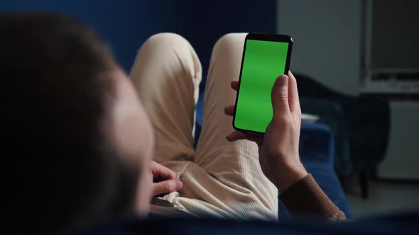 Man Lying on Couch Using Smart Phone with Chroma Key Green Screen at Night, Scrolling Through Social