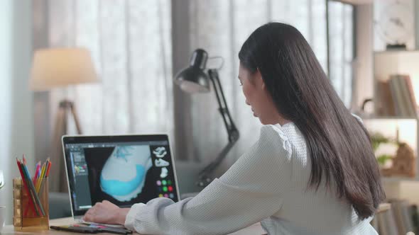 Asian Female Footwear Designer Thinking While Designing Shoe On A Laptop At Home