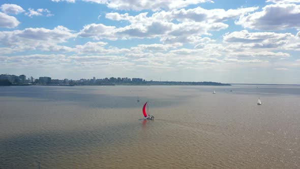 Drone shot. Sailing red boat, wind river and city.