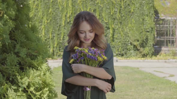 Portrait of Pretty Smiling Young Woman Holding Bouquet of Wild Flowers Looking at Camera