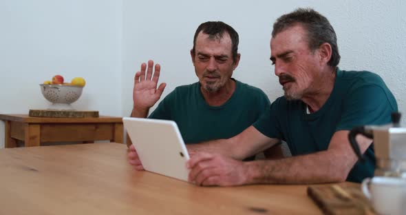 Twin brother senior men having fun on a video call with digital tablet at home