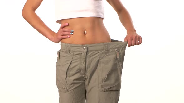 Sporty Girl in Big Trousers, Showing Her Lose Weight, on White