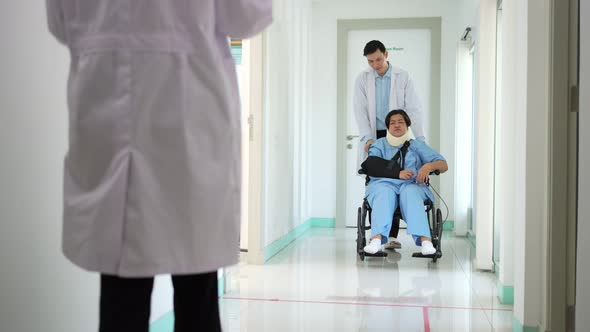 Asian woman patient in wheelchair after accident and talking with Doctor, surgeon pushing patient on