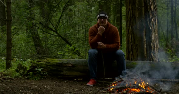 Muscular Guy in Brown Hoodie Looks at Bonfire in Forest