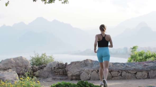 A Sporty Woman Runs Up to a Stone Fence and Jumps on It with Spreading Her Hands