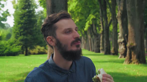 Man Eats a Sandwich with Salad in the Park