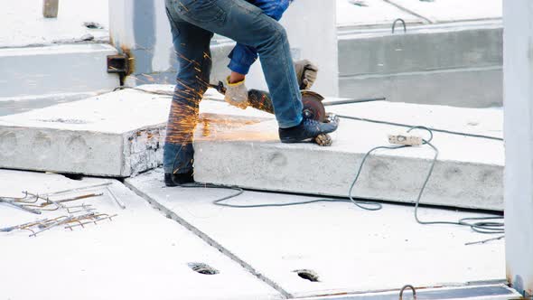 A professional builder cuts iron rebar with an angle grinder machine on a reinforced concrete slab
