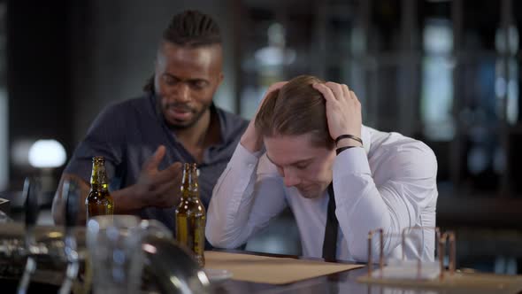 Frustrated Caucasian Man Holding Head in Hands As African American Friend Cheering Up Mate