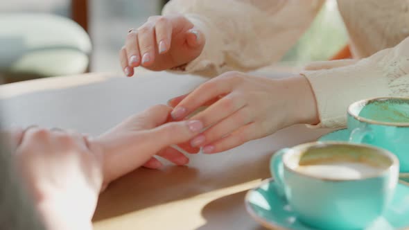 Two Unrecognizable Young Caucasian Women Holding Hands Sitting in Cafe with Coffee Cups