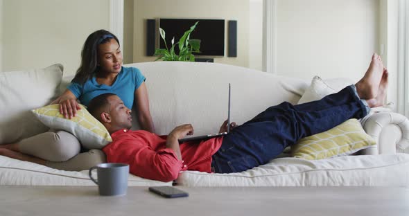 Happy biracial couple on sofa with laptop and talking