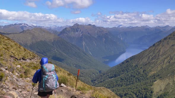 Static, hiker walks along exposed alpine path, distant lake and mountain landscape, Kepler Track New