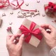 Woman's hands wrap christmas present in craft paper with red ribbon and berries. - VideoHive Item for Sale