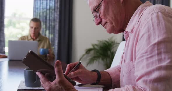 Caucasian senior taking notes while using digital tablet at home