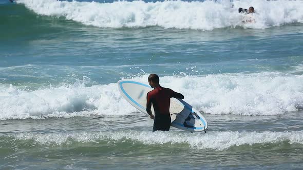 Man in Surfing Costume Entering Ocean, Carrying Board in Hands, Active Sport