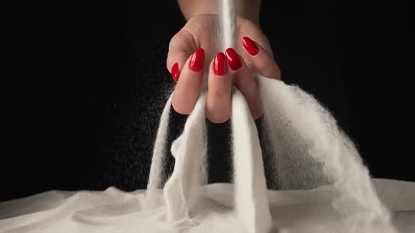 Woman with Handful of White Dry Sand in Her Hands Spilling Sand Through Her Fingers on Black Studio