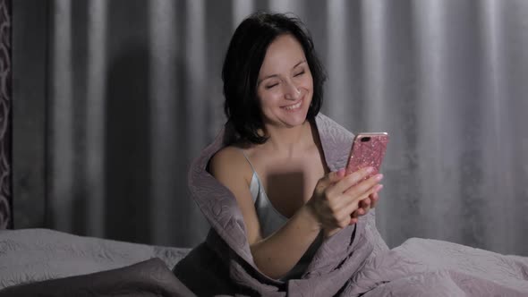 Woman Sitting on Bed Under Blanket, Enjoying Video Chat To Friend on Smartphone