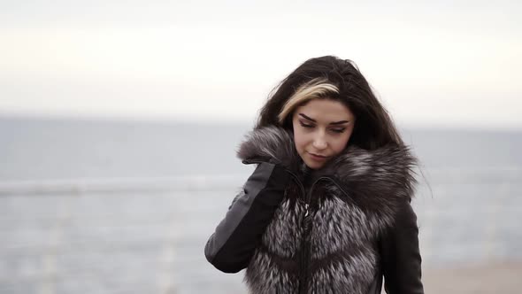 Portrait of a Young Brunette Woman Walking By the Sea or Ocean in Winter Wearing Fur Coat