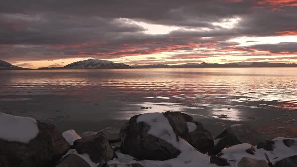 Snowy scene during sunset reflecting over lake in winter