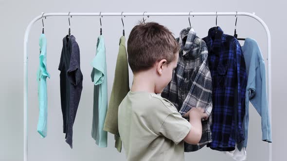 Boy preschooler standing by the hangers, racks up clothes, and chooses clothes for today.