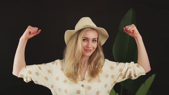 Funny Confident Young Blonde Caucasian Woman in White Dotted Shirt and a Hat Tightening Her Biceps