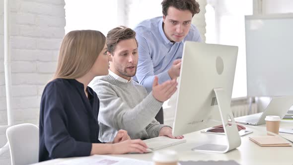 Worried Creative Professional Discussing with Team and Using Desktop