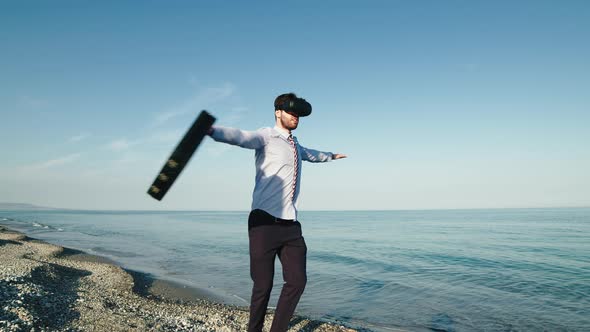 Happy Business Guy Spins on Himself with Virtual Reality Glasses on the Beach