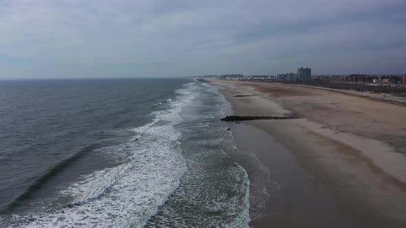 An aerial view of an empty beach on a cloudy day. The camera dolly in over the ocean as the waves ge