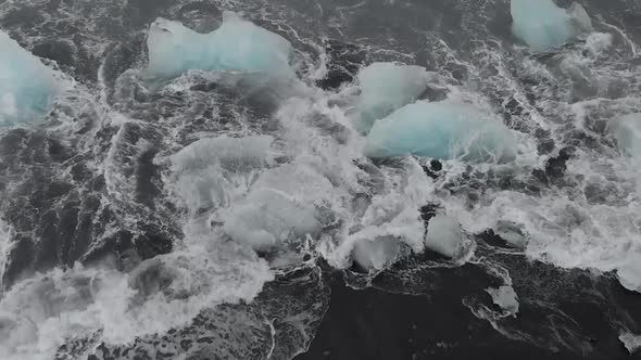 4K shot of waves crashing into icebergs on black sand beach.