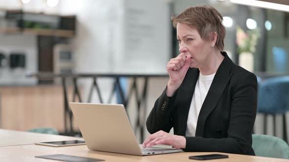 Sick Old Businesswoman with Laptop Coughing in Office 