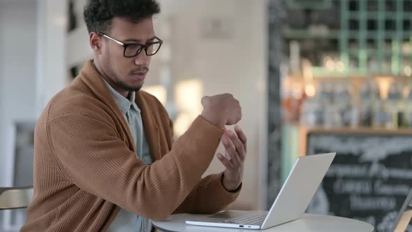 African Man Having Wrist Pain While Using Laptop in Cafe