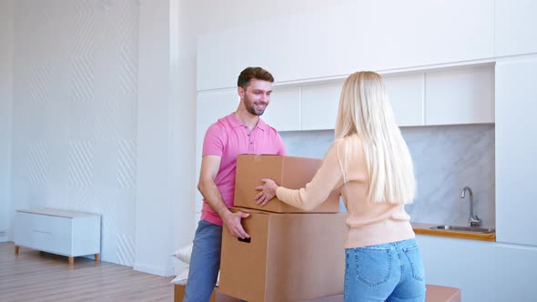 Young woman blonde with long loose hair helps bearded man carry large brown boxes