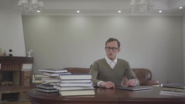 Young Modestly Dressed Man in Glasses Sitting at the Wooden Table in the Office