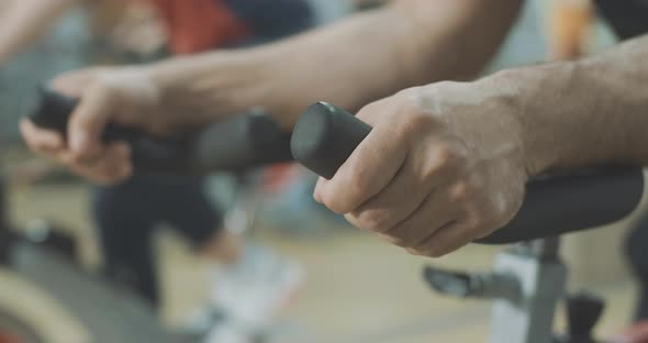 Close-up of Male Caucasian Hands Putted on Handlebar of Exercise Bike in Gym. Unrecognizable Young