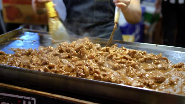 Chef stirring meat stew on an open flat grill, train night market Bangkok