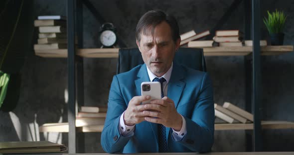 Shocked Senior Business Man Reacting on Bad Message on Smartphone Reading Terrible New While Sitting