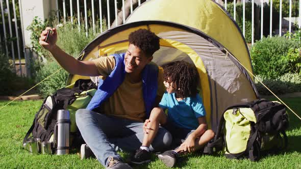 Happy biracial man and his son taking selfies using smartphone in garden