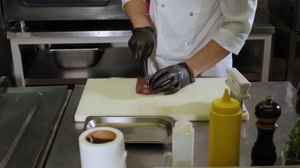 Male Chef Cutting Piece of Beef on Wooden Board in Restaurant Kitchen