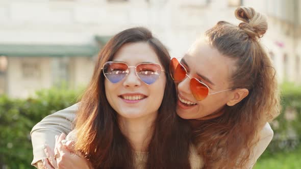 Portrait of Two Young Smiling Hipster Women Friends Wearing Sunglasses of Heart Shape. Lesbian Girls