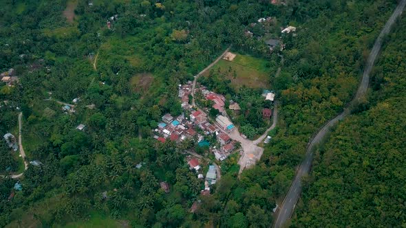 Bird's eye aerial over a small village in a forest-covered valley with a camera tilt up to reveal su