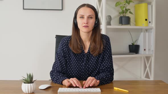 Modern Businesswoman Wearing Headset is Typing and Looks at the Camera
