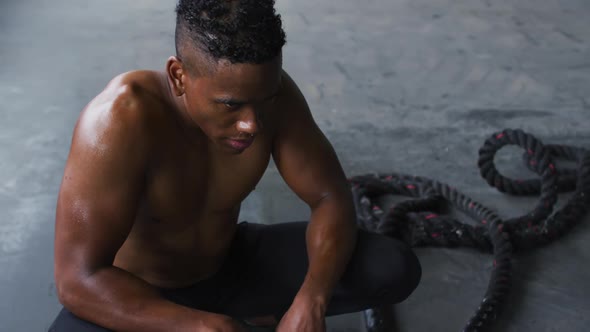 Shirtless african american man resting after battling ropes in an empty urban building