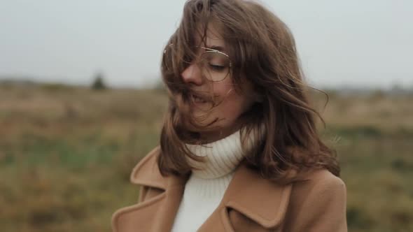 A Gentle Young Woman Stands on the Background of Nature in an Autumn Coat and Corrects Her Hair