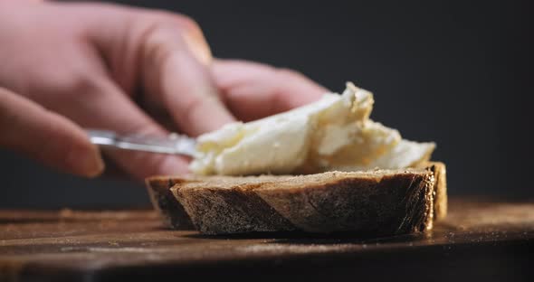 Woman Puts Fresh Cream Cheese on Rye Bread on Wooden Table